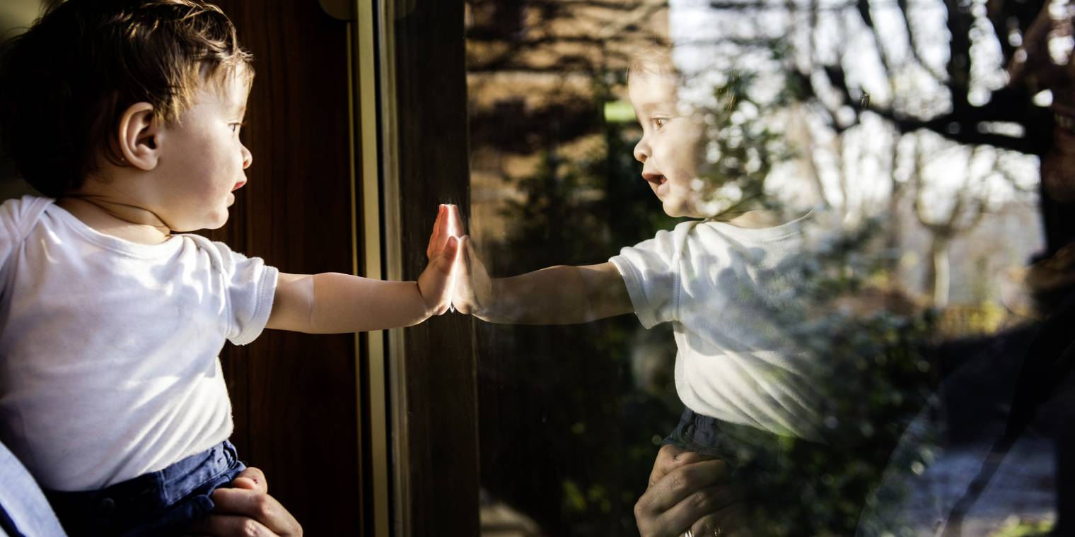 Baby boy in fathers arms looking through and touching window